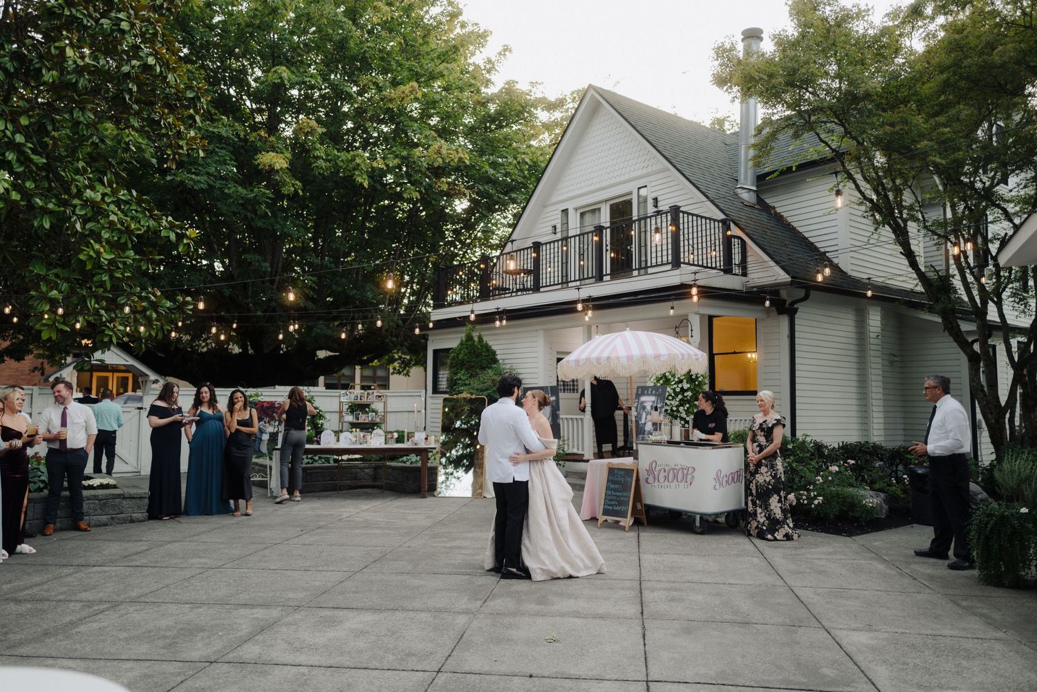 An outdoor wedding reception venue with string lights and white tents set up in a garden setting.