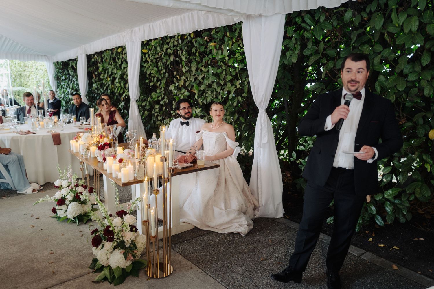 Wedding reception venue decorated with white draping, greenery, and golden candlesticks.