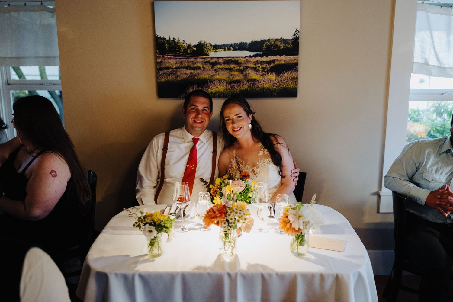 Reception dining table set with bright floral centerpieces in warm-lit indoor venue.