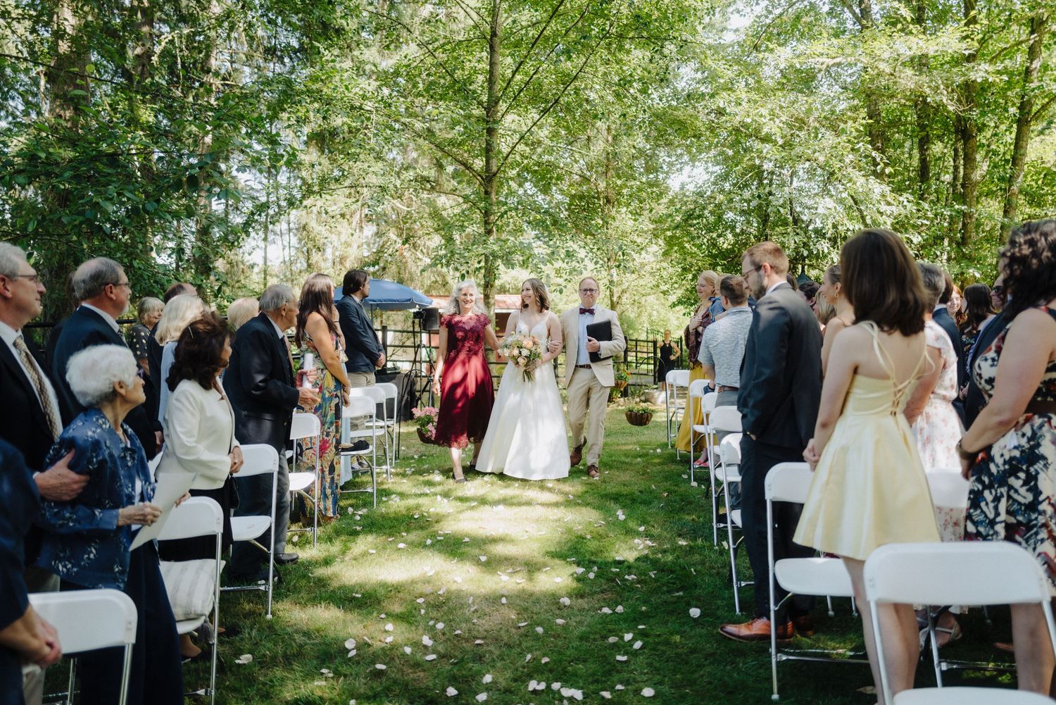Panoramic view of wedding guests seated in white chairs during an outdoor garden ceremony.