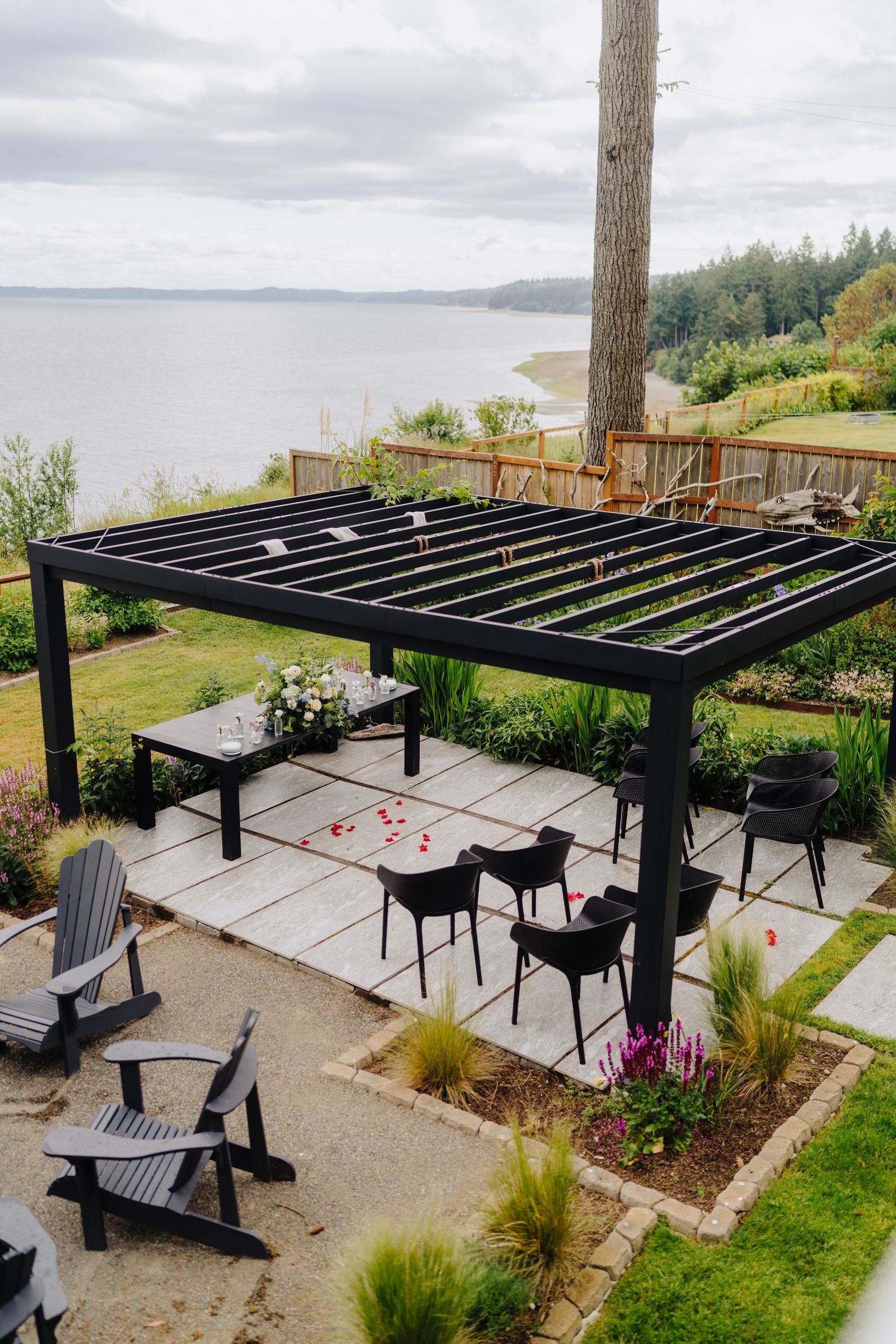 Modern black pergola construction process showing installation stages on an oceanfront patio with Adirondack chairs.