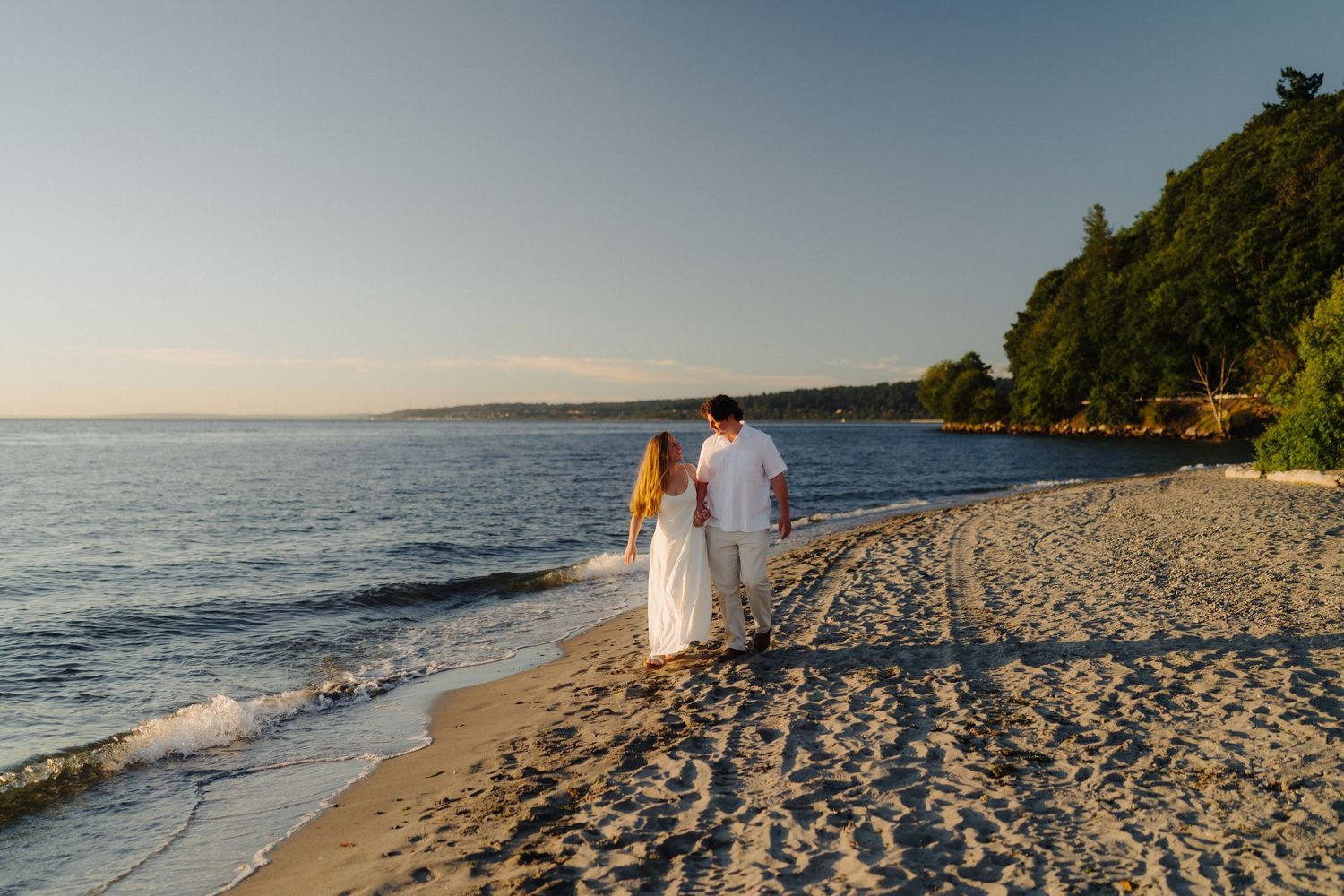 Couple walking along a pristine beach with rocky cliffs and ocean views.