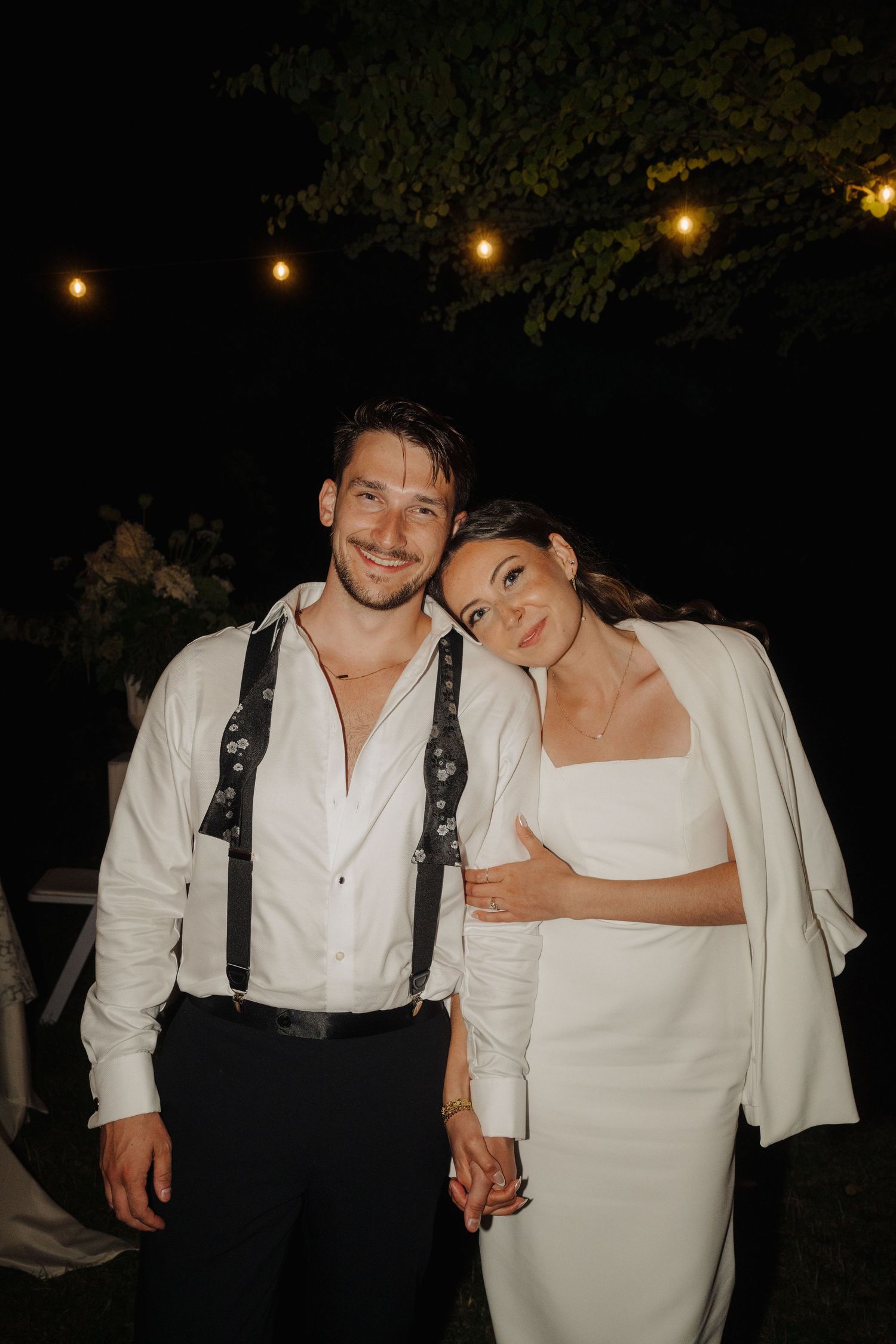 A romantic evening wedding photo with string lights illuminating a couple in formal attire.