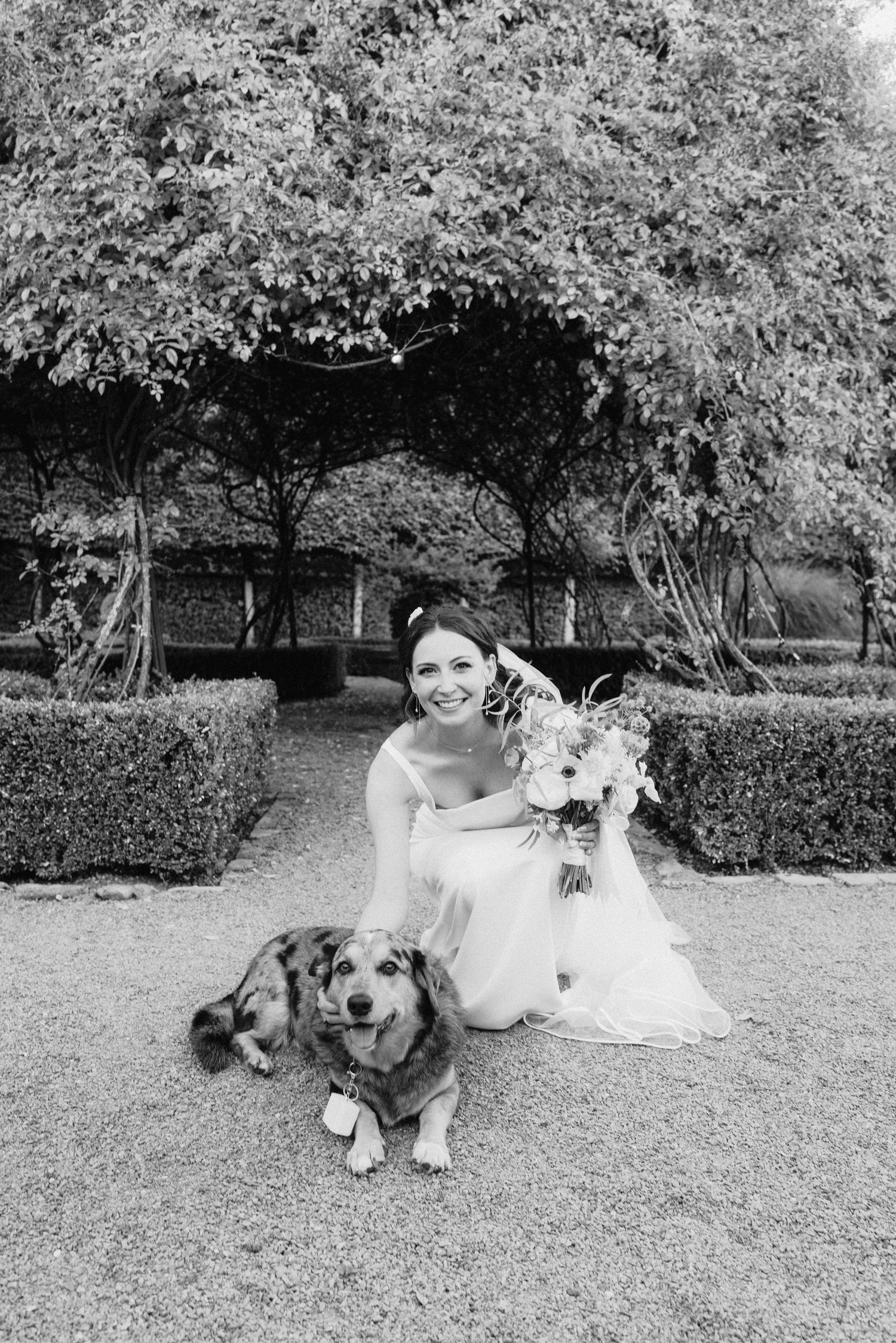 Black and white photo of wedding party relaxing on grass with dogs.