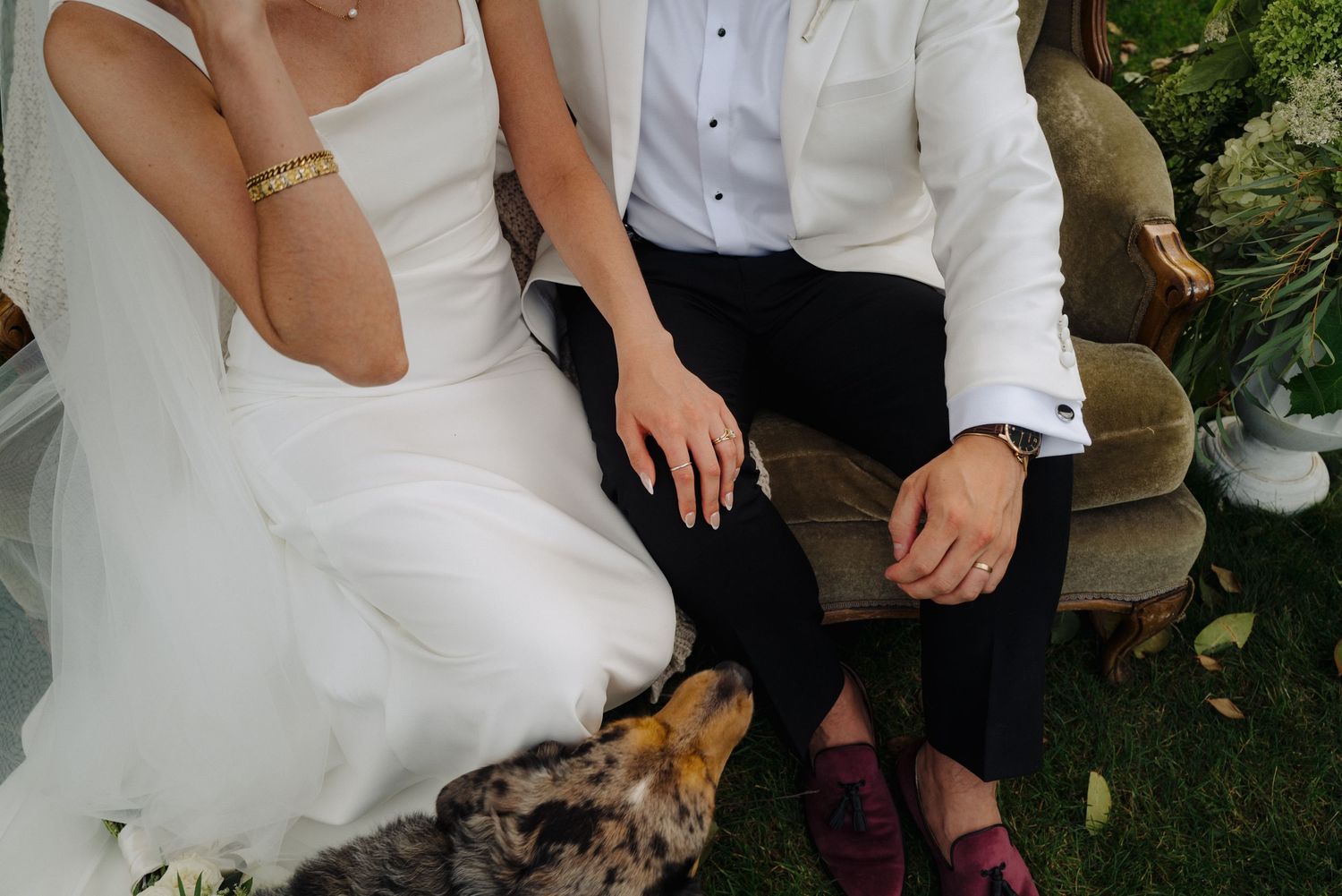 Couple in wedding attire sits together on outdoor furniture during a garden celebration.