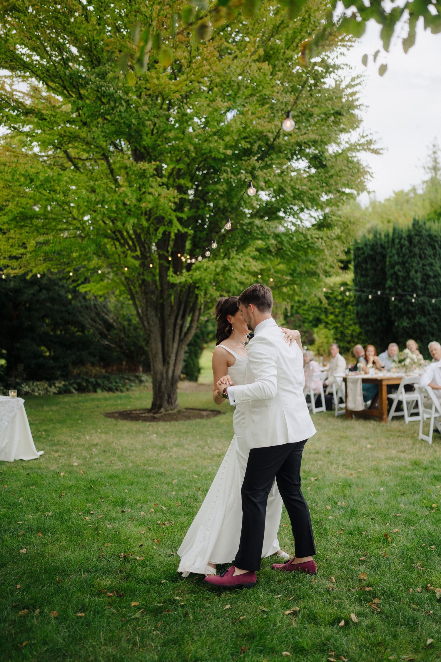 Romantic first dance under green trees at outdoor garden wedding.