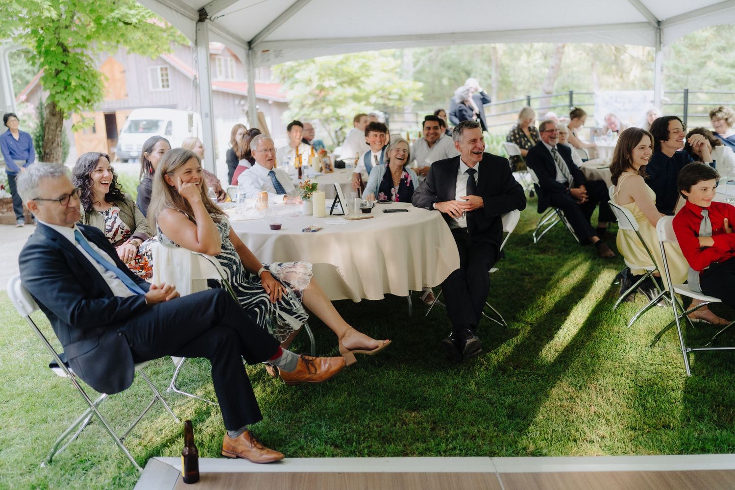 Wedding guests seated at round tables under a white tent during an outdoor reception.
