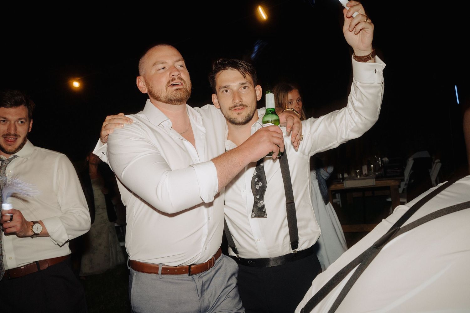 Wedding guests dance and celebrate at a dimly lit evening reception.