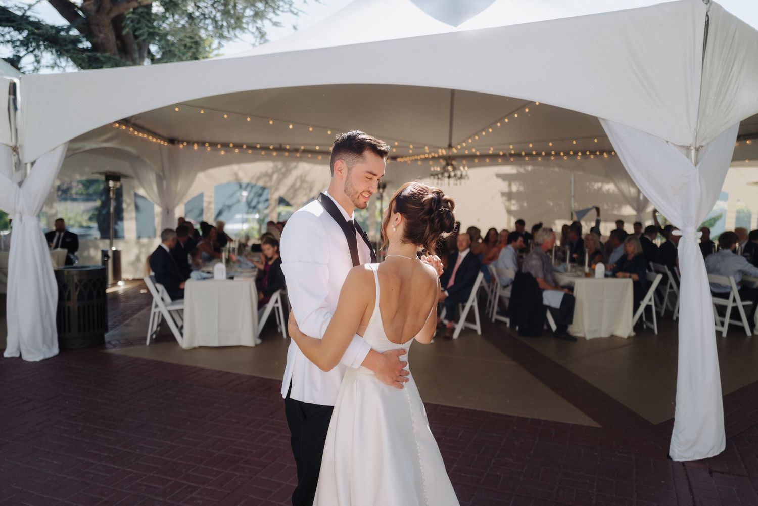Elegant wedding reception setup under white tent pavilions with string lights and table settings.