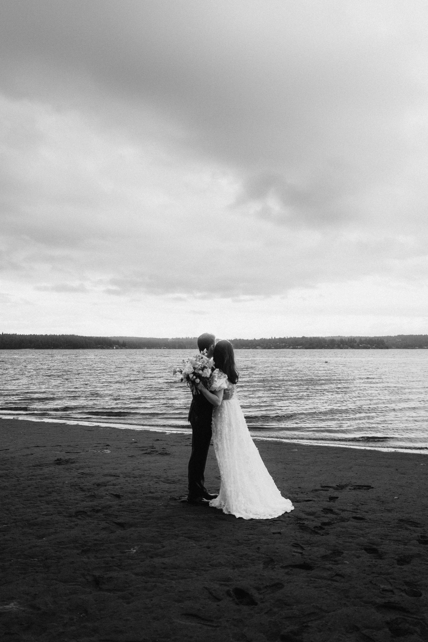 A romantic black and white beach wedding portrait with dramatic cloudy skies.