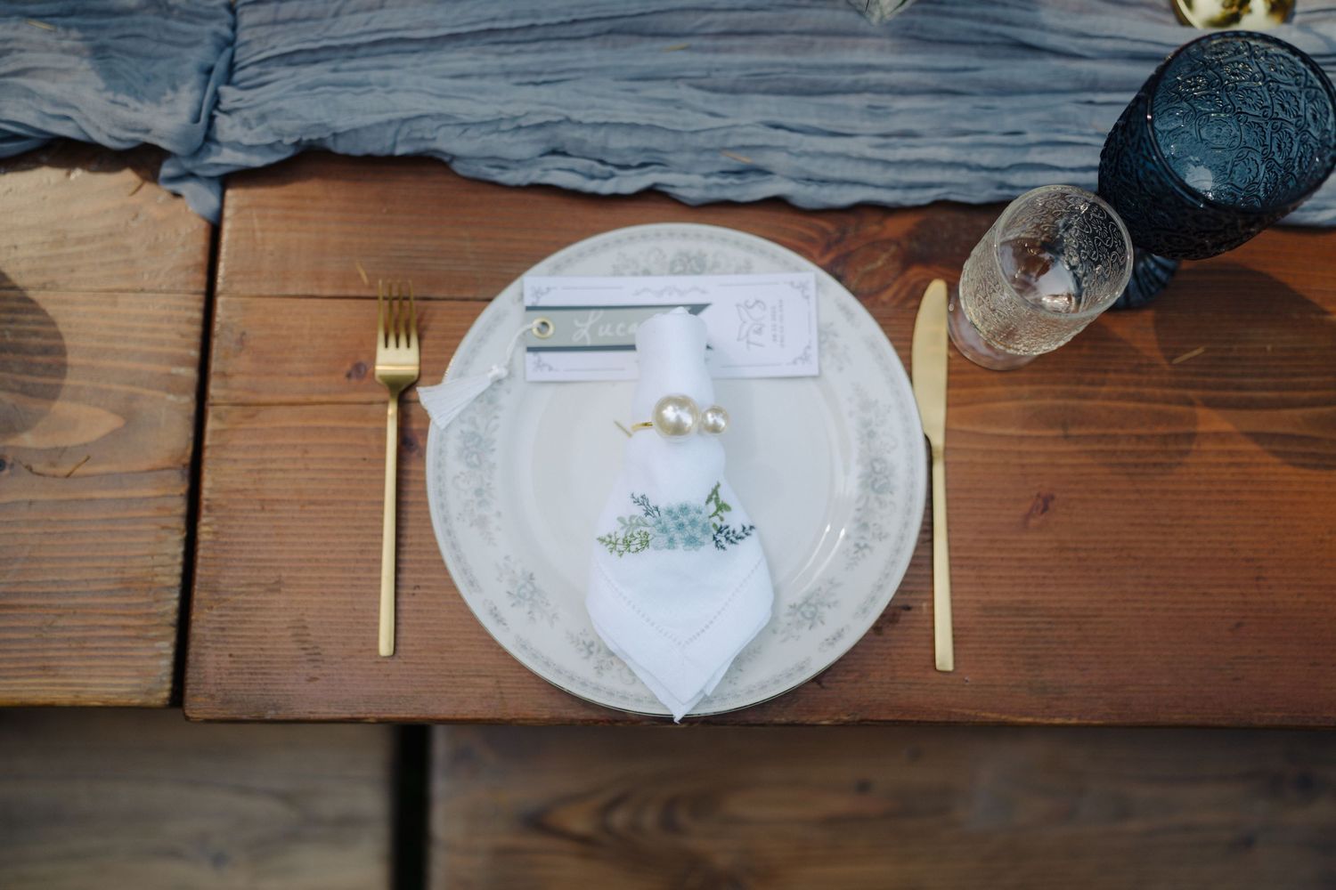 Place setting with gold utensils and decorative plate on wooden table.