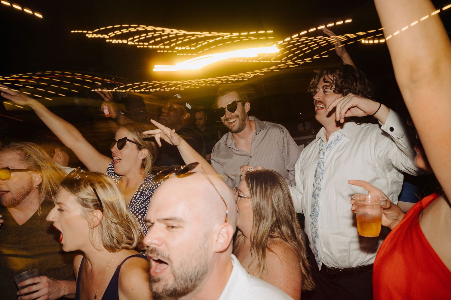 Wedding reception dance floor filled with guests celebrating under warm string lights.