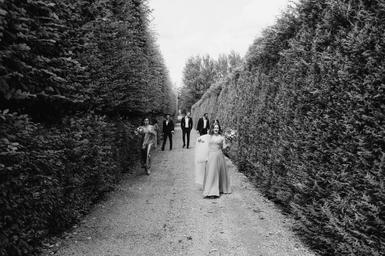 Black and white photo of people walking along a tree-lined path.