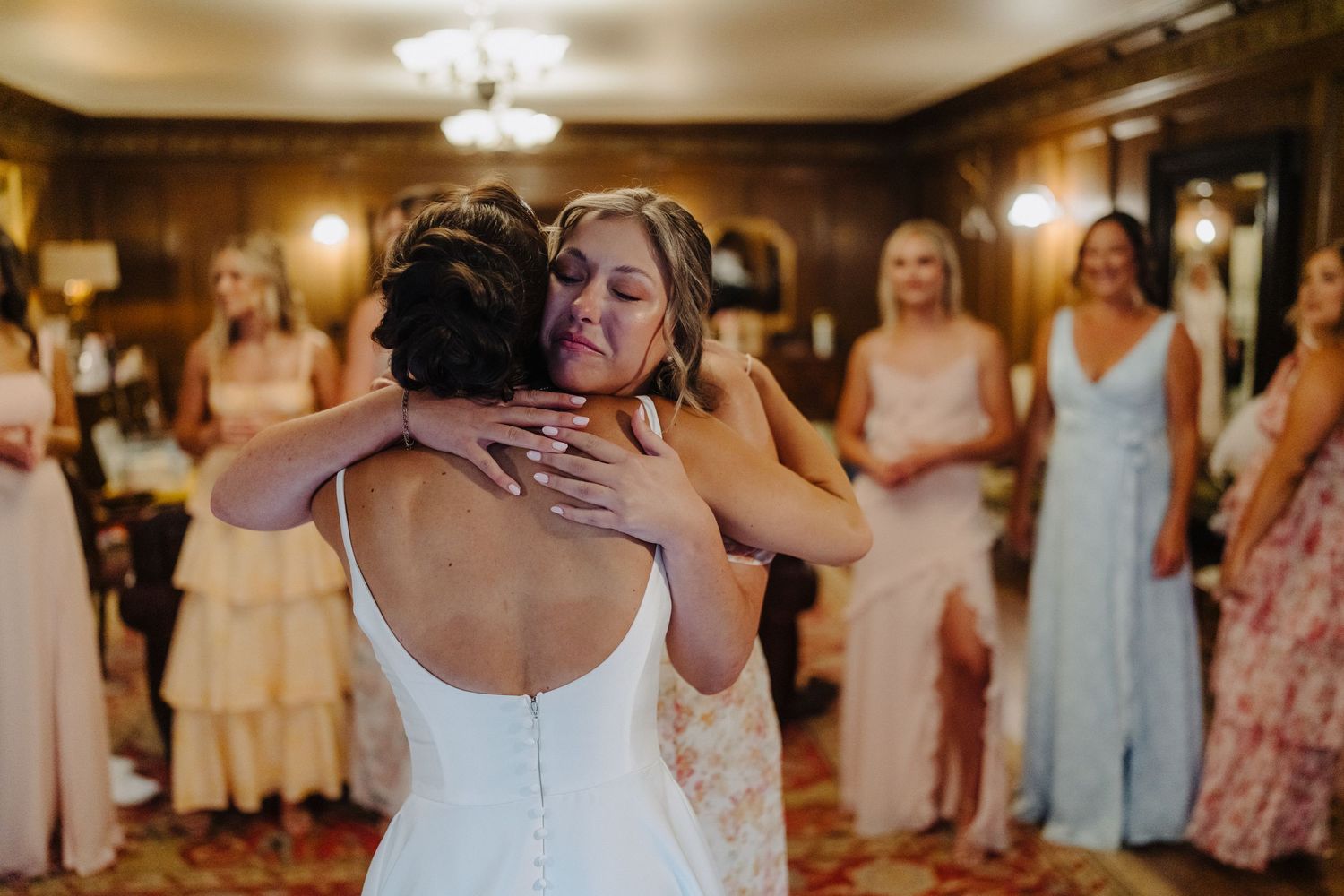 An emotional embrace during a wedding celebration with guests looking on in formal attire.