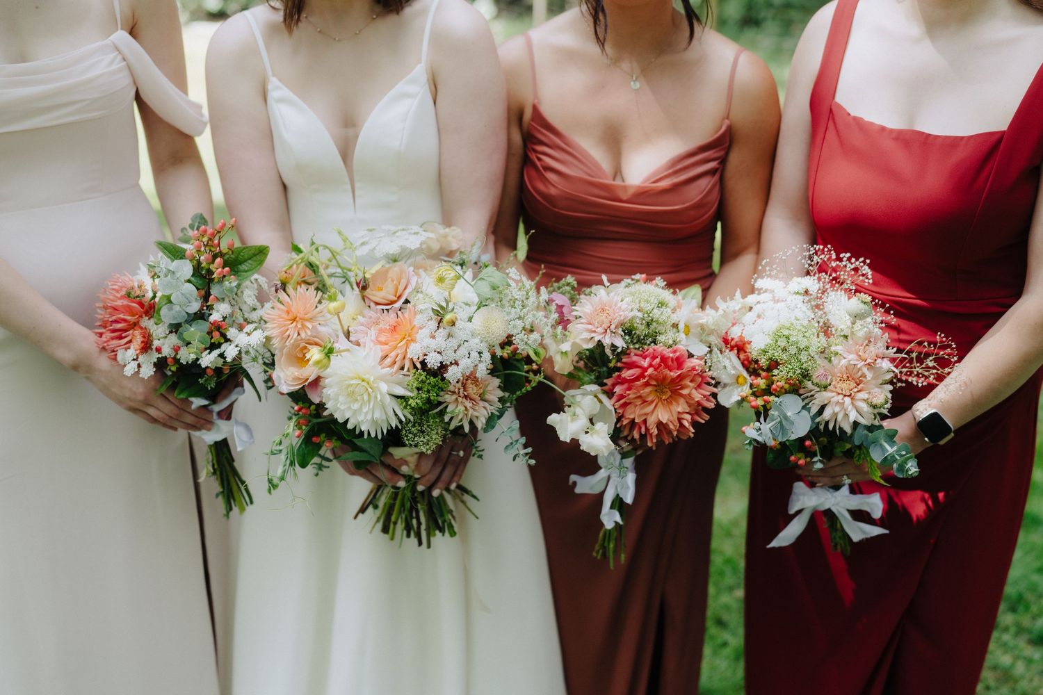 Row of bridesmaids holding colorful floral bouquets featuring coral and white blooms.