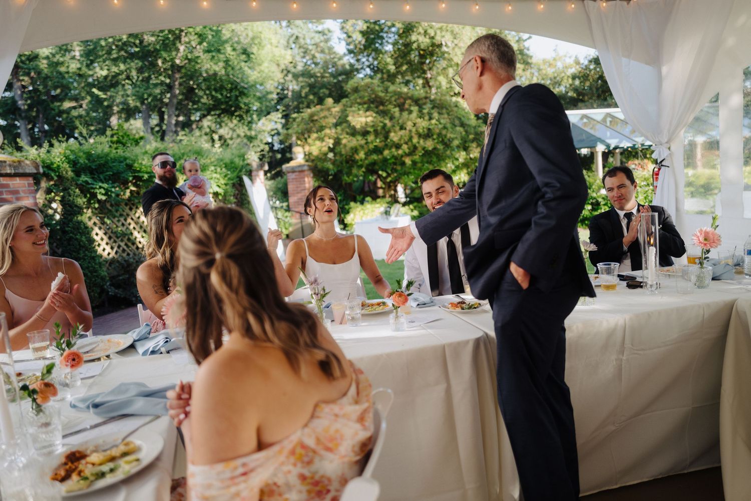 Wedding guests enjoying the reception under an elegant white tent outdoors.