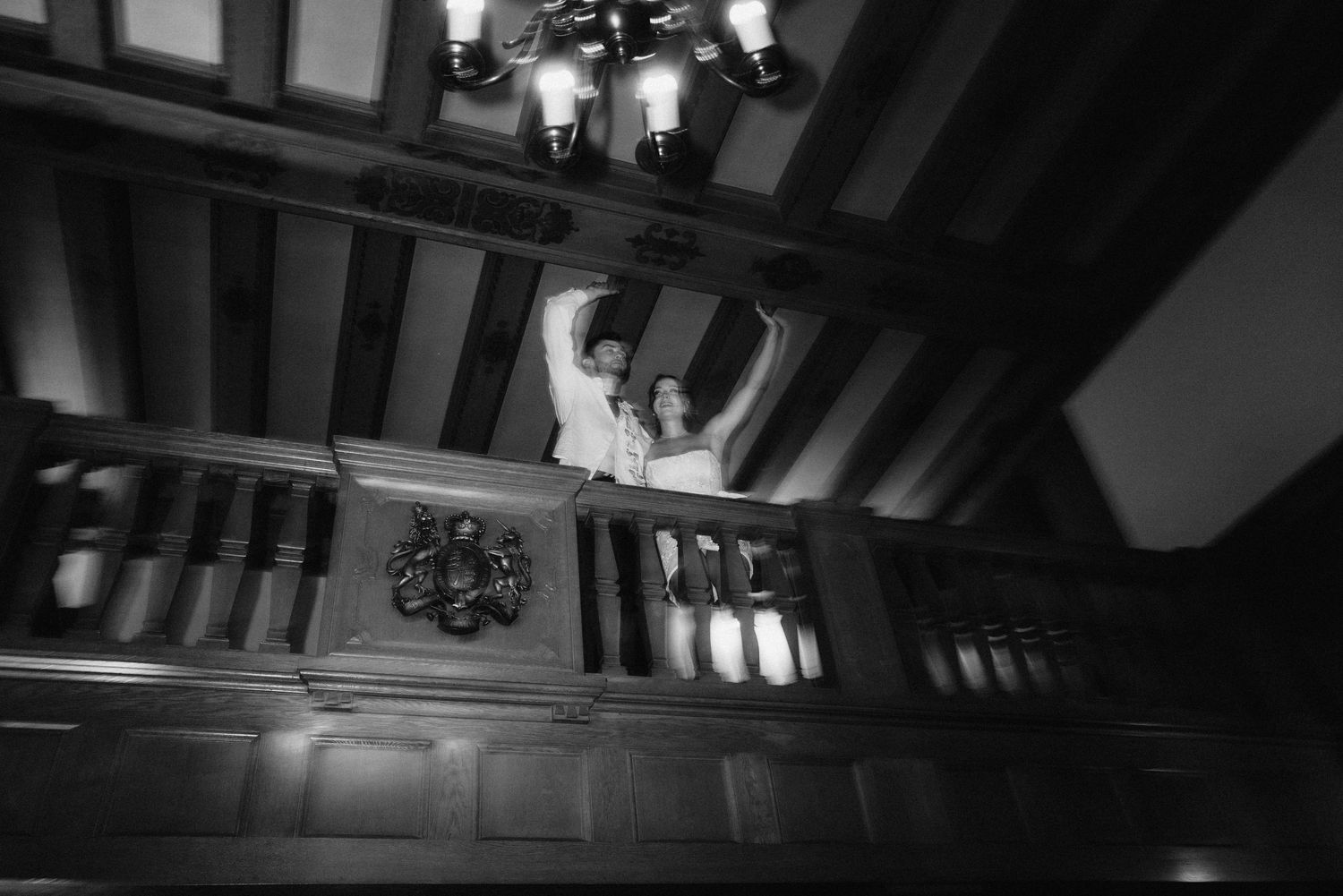 Dramatic black and white view looking up at an ornate staircase with chandelier in historic mansion.