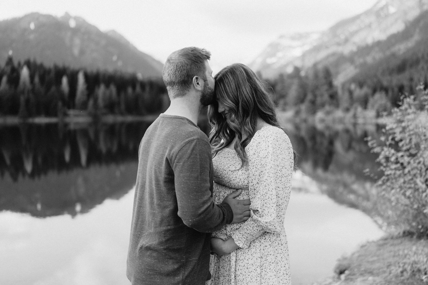 Black and white maternity photo capturing tender moment against mountain landscape.