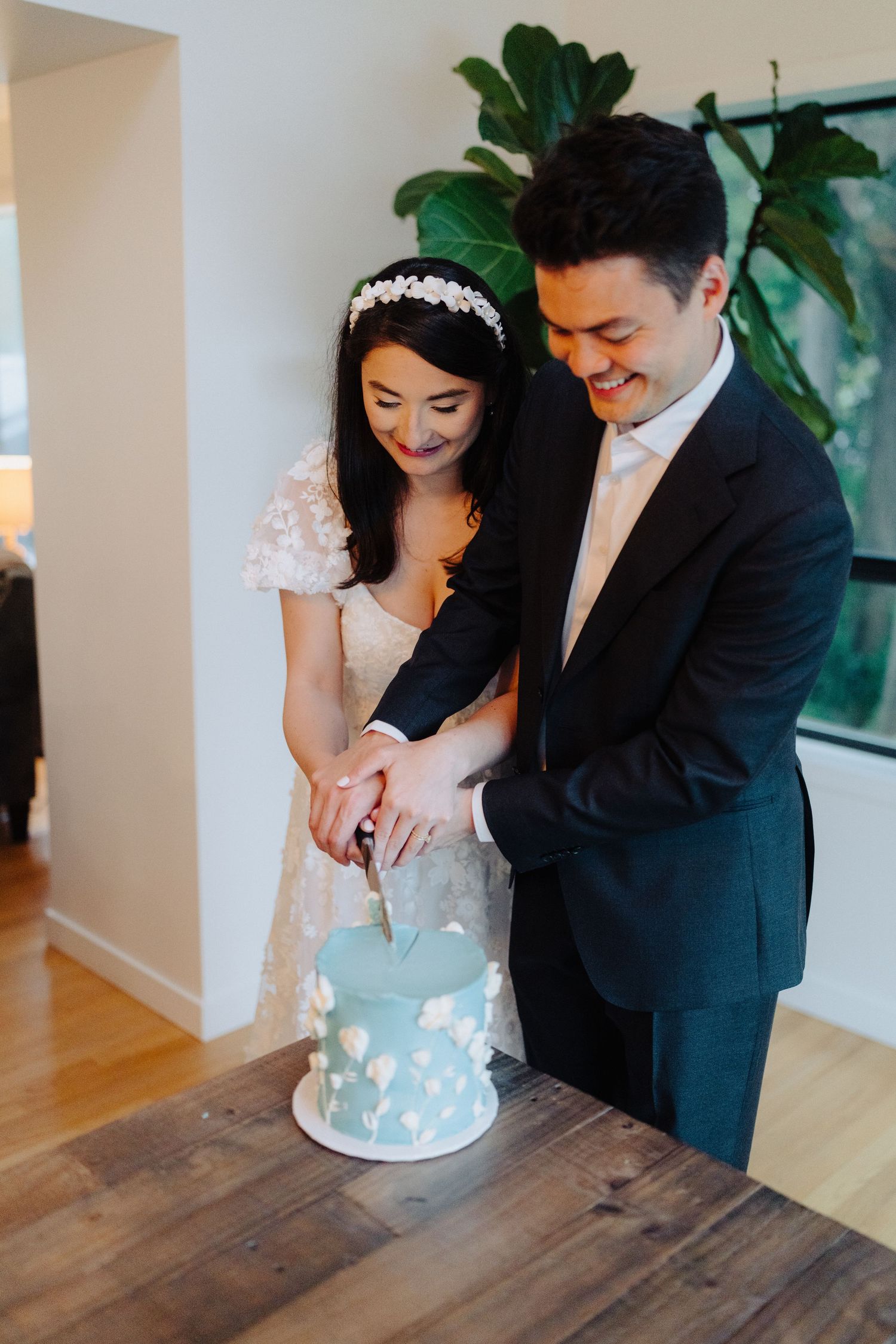 Newlyweds cutting into a light blue wedding cake together at their reception.