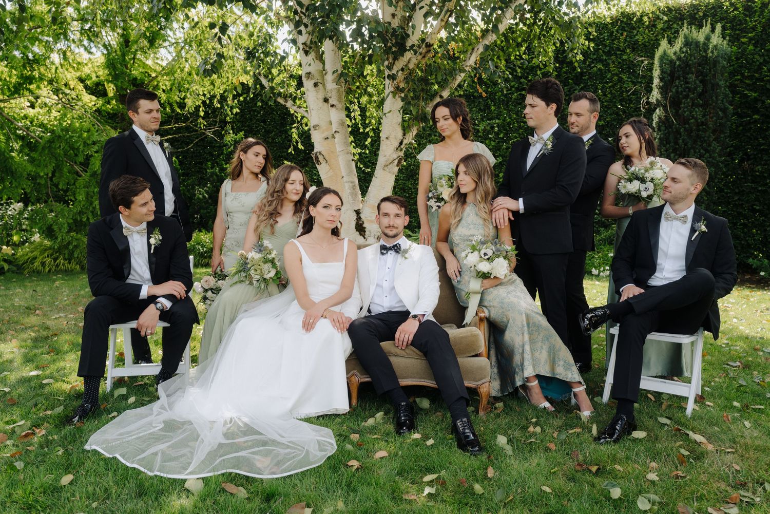 Wedding party relaxing on grass during outdoor photo session in garden setting.