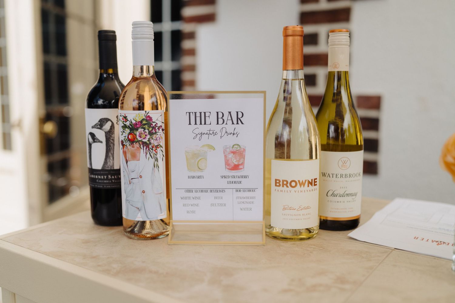 A wedding bar setup featuring wine bottles and a decorative menu sign.