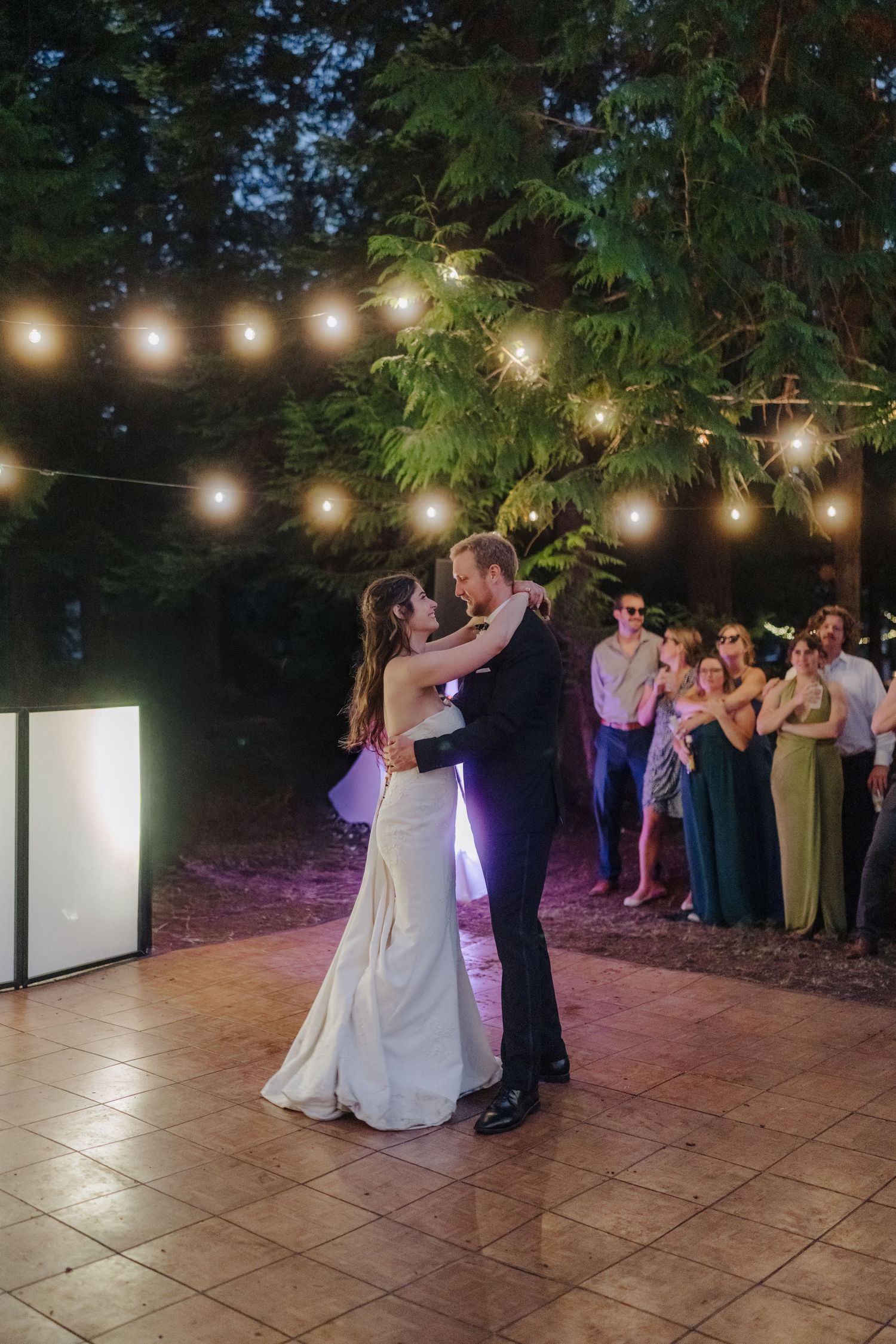 Evening wedding reception with string lights illuminating couples dancing on a stone patio.