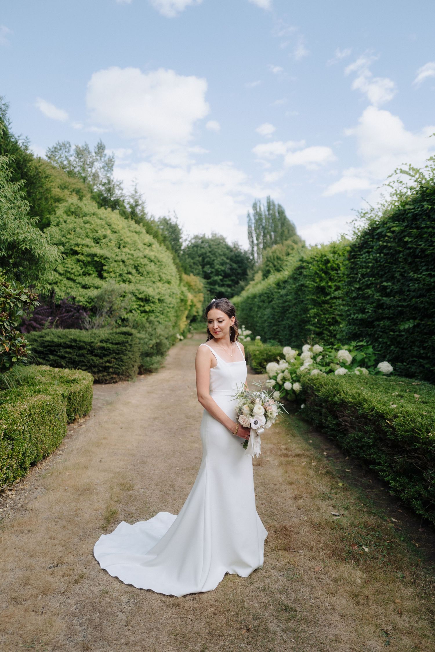 Garden path with white flowers and hedges creates romantic wedding backdrop.
