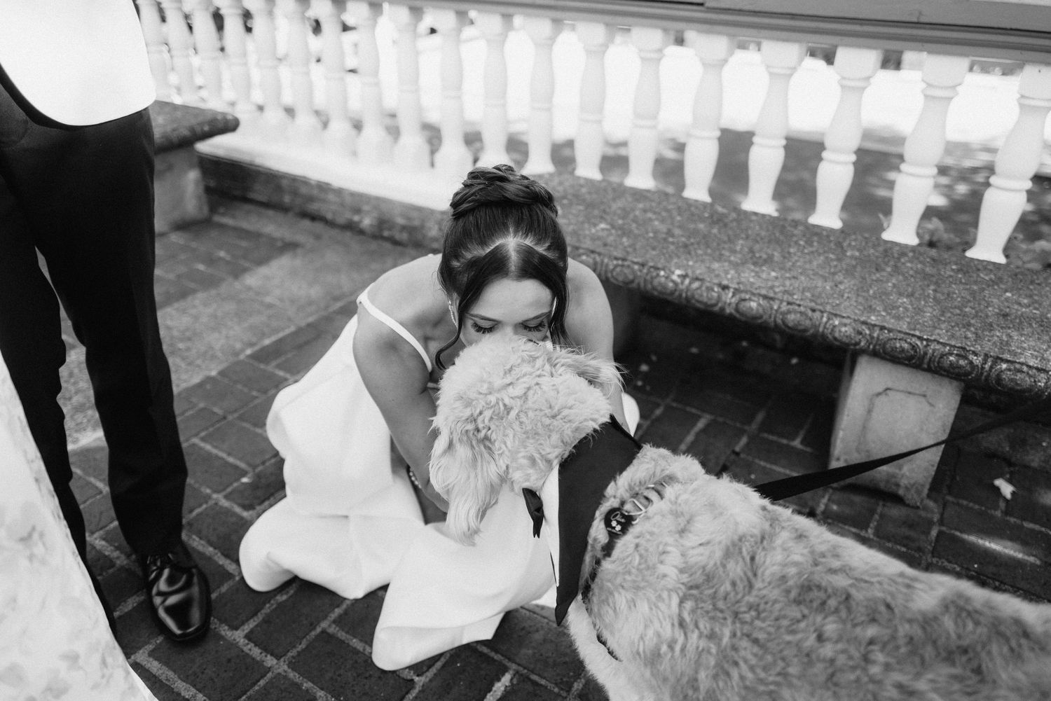 A person in a wedding dress bends down to pet a dog on outdoor steps.