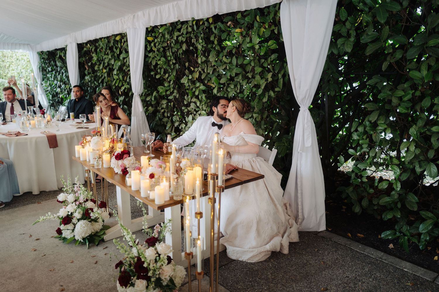 Elegant wedding reception space with white drapes, floral arrangements and candlelit tables.