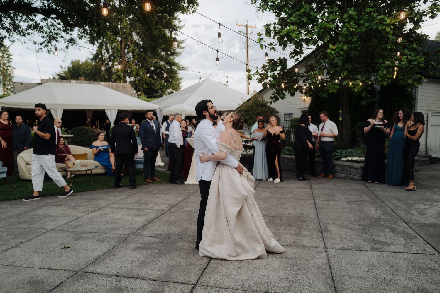 Wedding party and guests enjoying outdoor reception on illuminated patio.