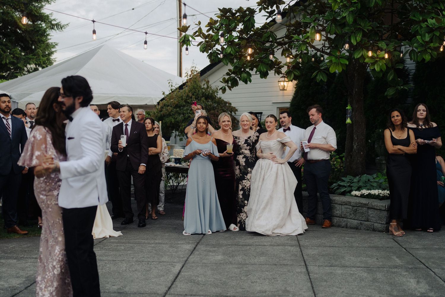 Outdoor wedding reception with string lights and white tent canopy during golden hour.