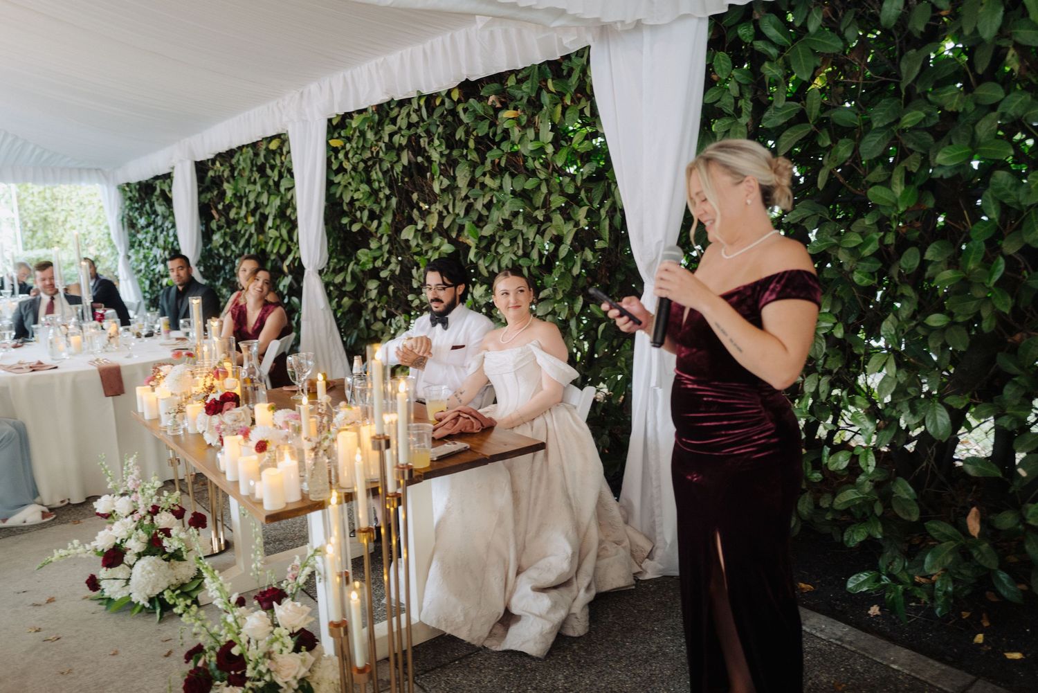 Wedding reception under white drapes with ivy walls and glowing candlelight on elegant tables.
