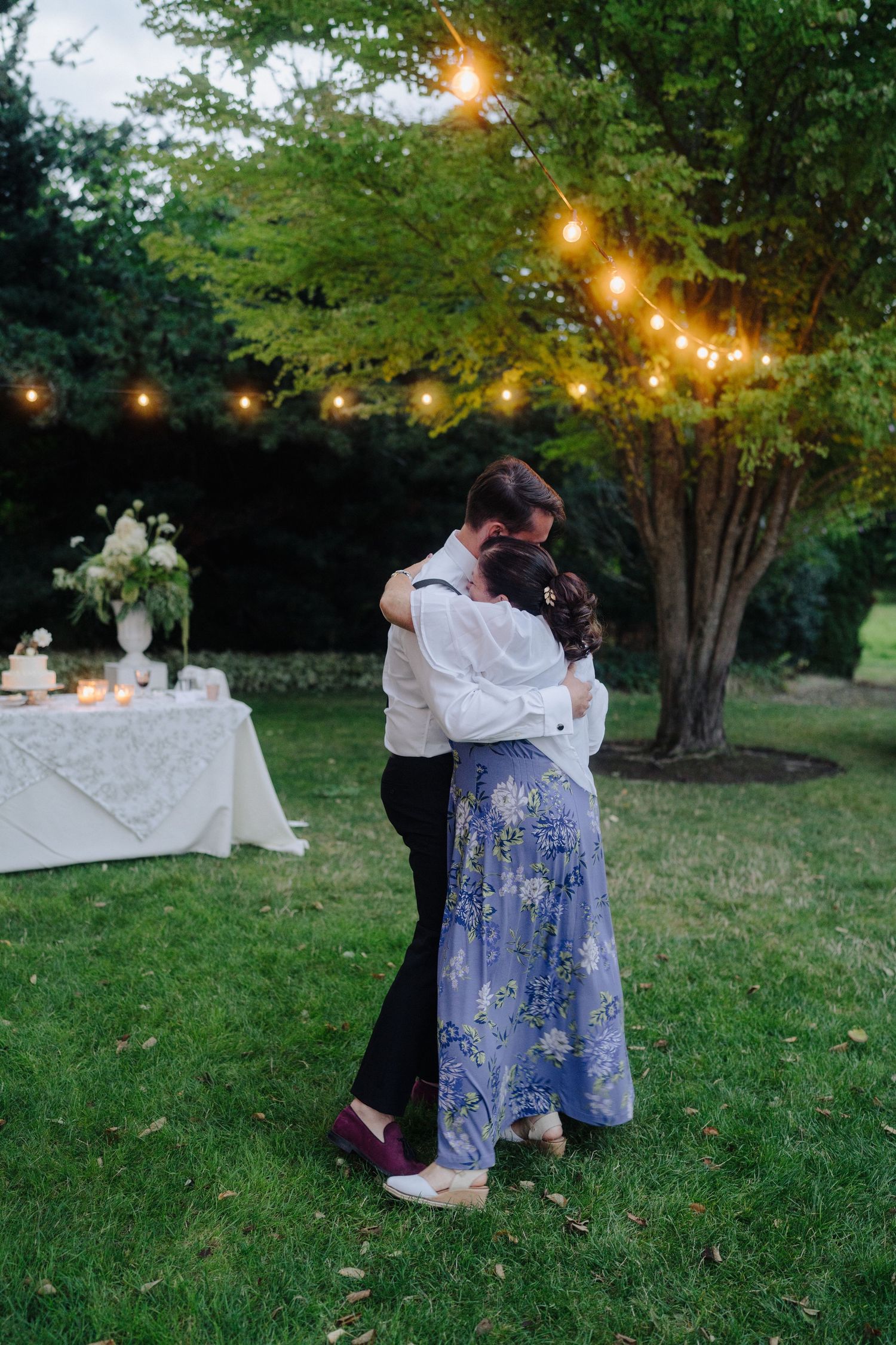 Couples dancing under string lights at dusk during an outdoor wedding reception.