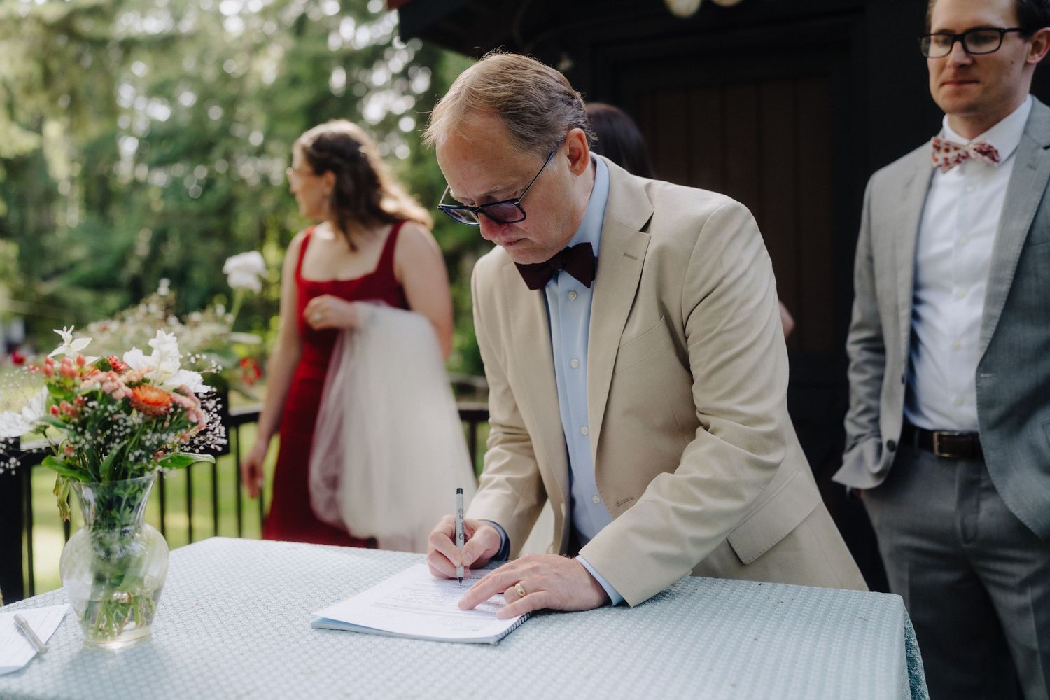 Wedding guests signing official documents at an outdoor ceremony table.