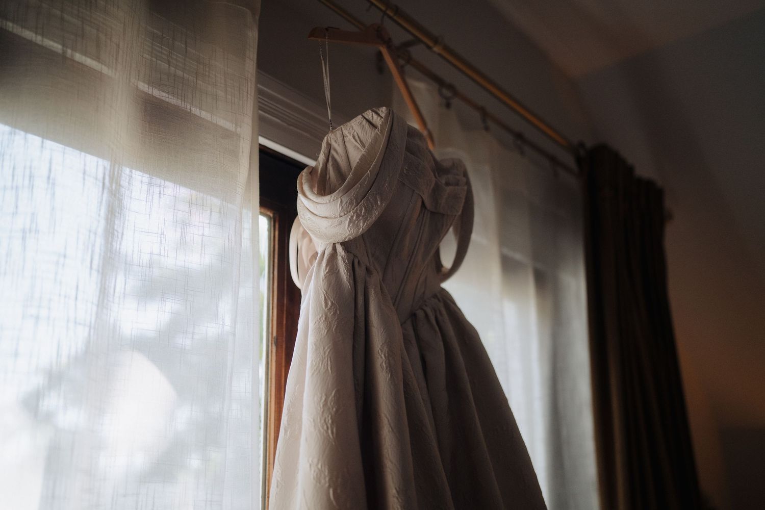 White wedding dresses hang elegantly in a row by sunlit windows creating a dreamy bridal preparation scene.