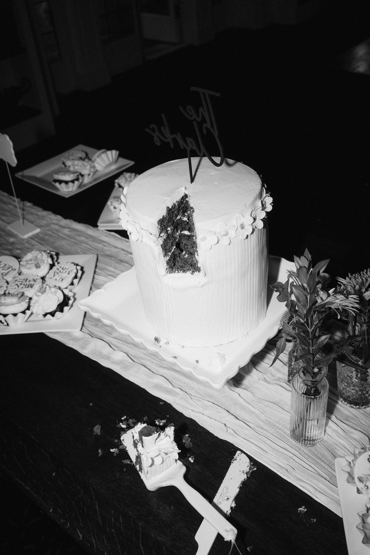 A white wedding cake with textured frosting and floral decorations displayed on a wooden surface.