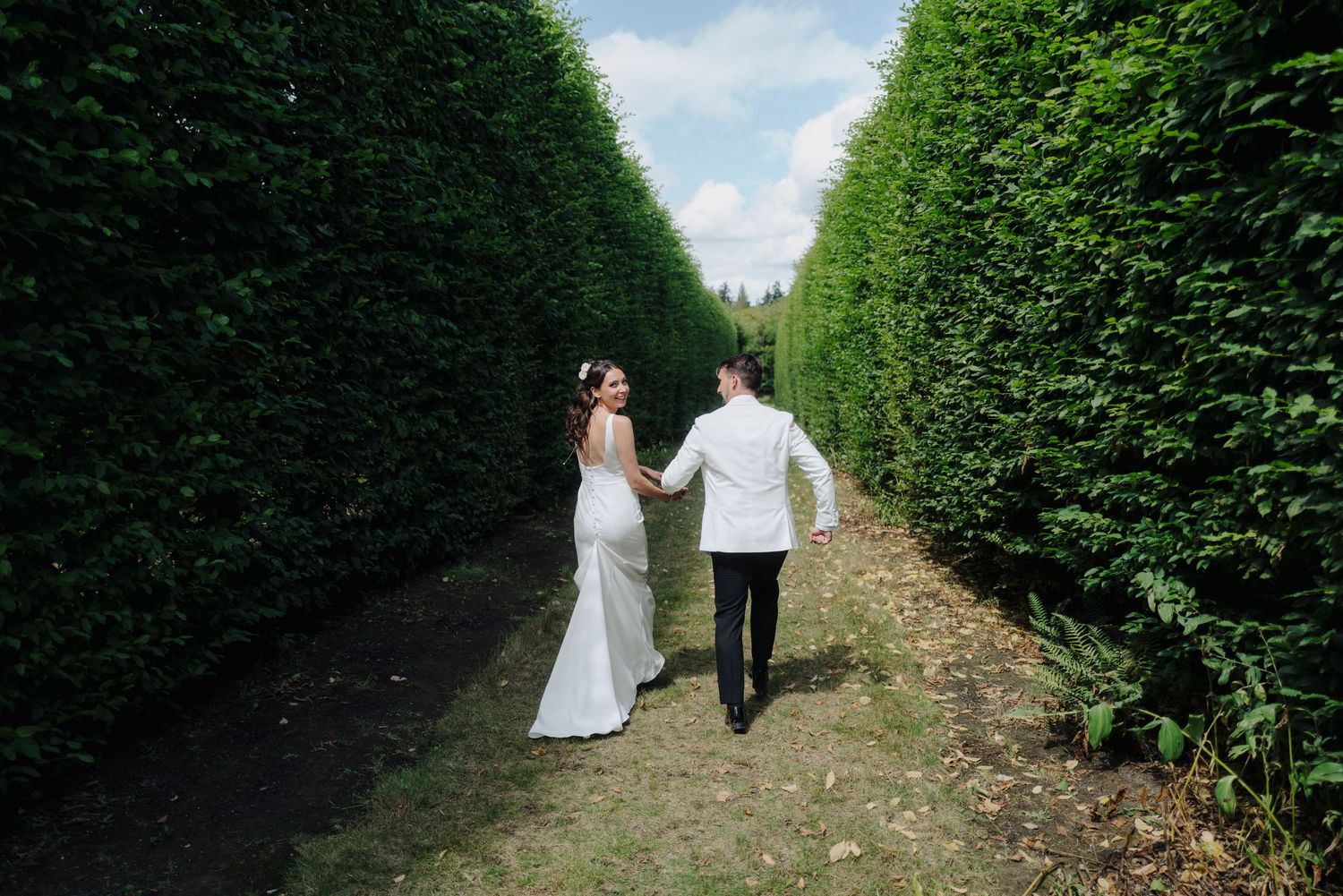 Wedding couple walking through a manicured hedge garden pathway.