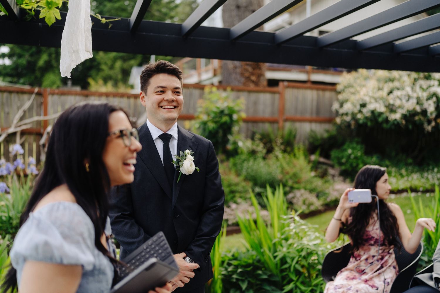 Wedding party gathers in a lush garden setting with white floral arrangements and decorative elements.