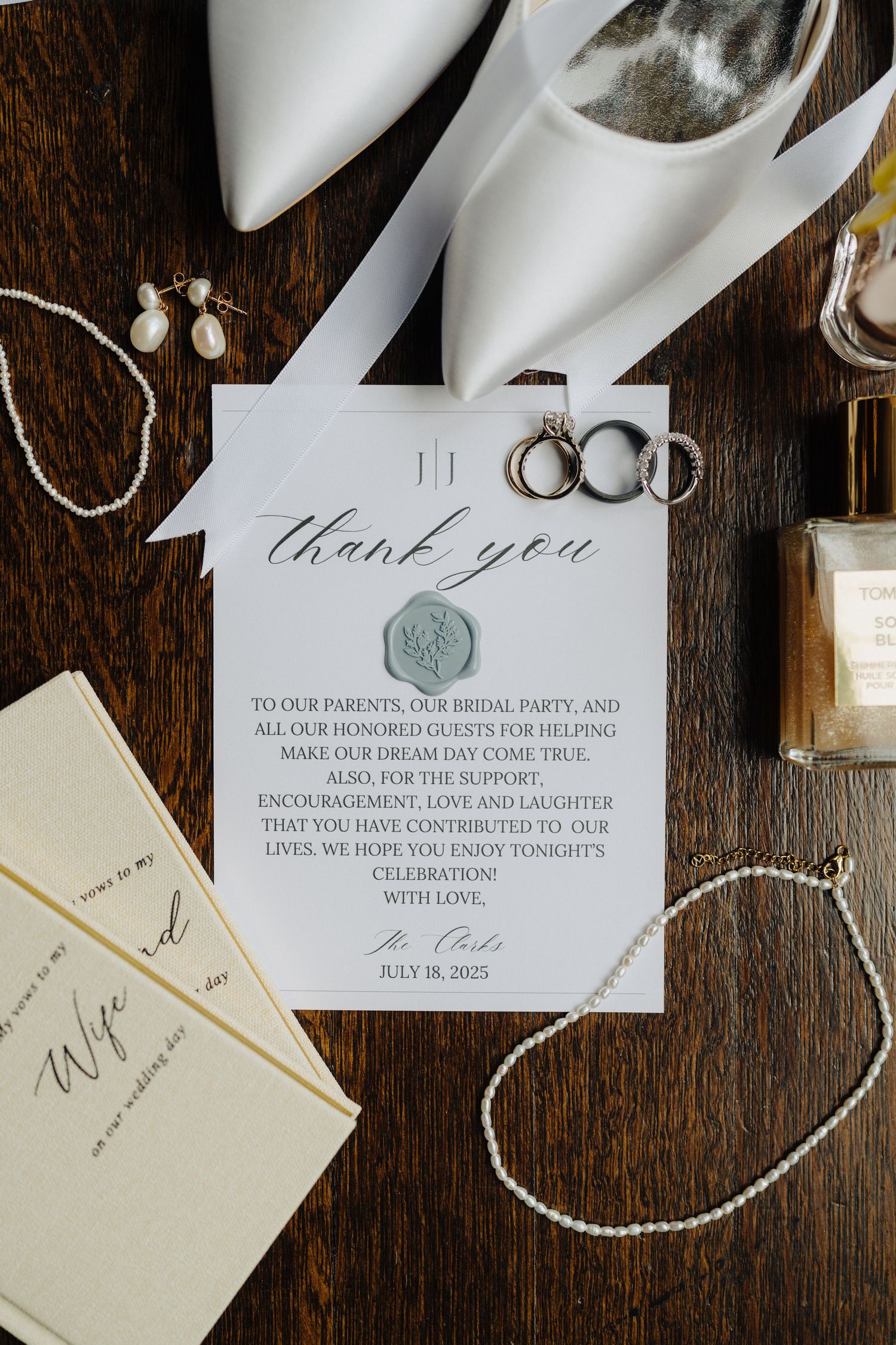 Wedding stationery and rings arranged on dark wooden surface with elegant calligraphy and wax seals.