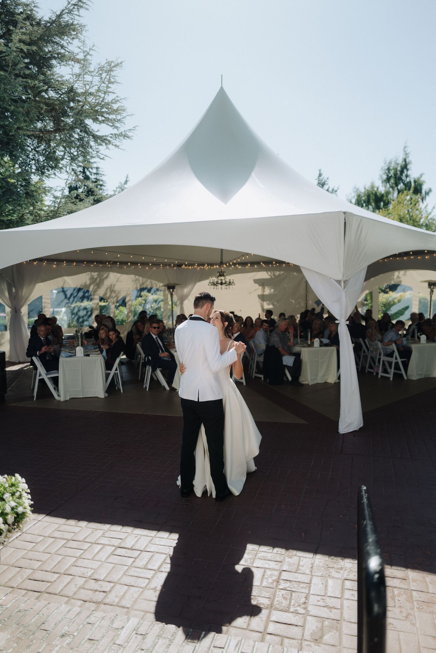 Outdoor wedding venue with white peaked tents and arranged seating on stone pavers.