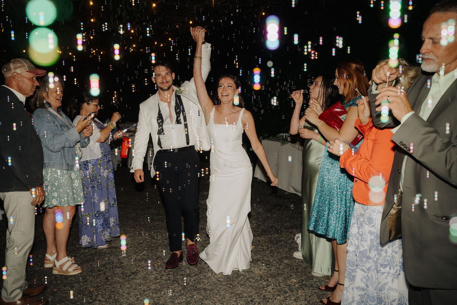 Wedding guests dancing under string lights at nighttime celebration.