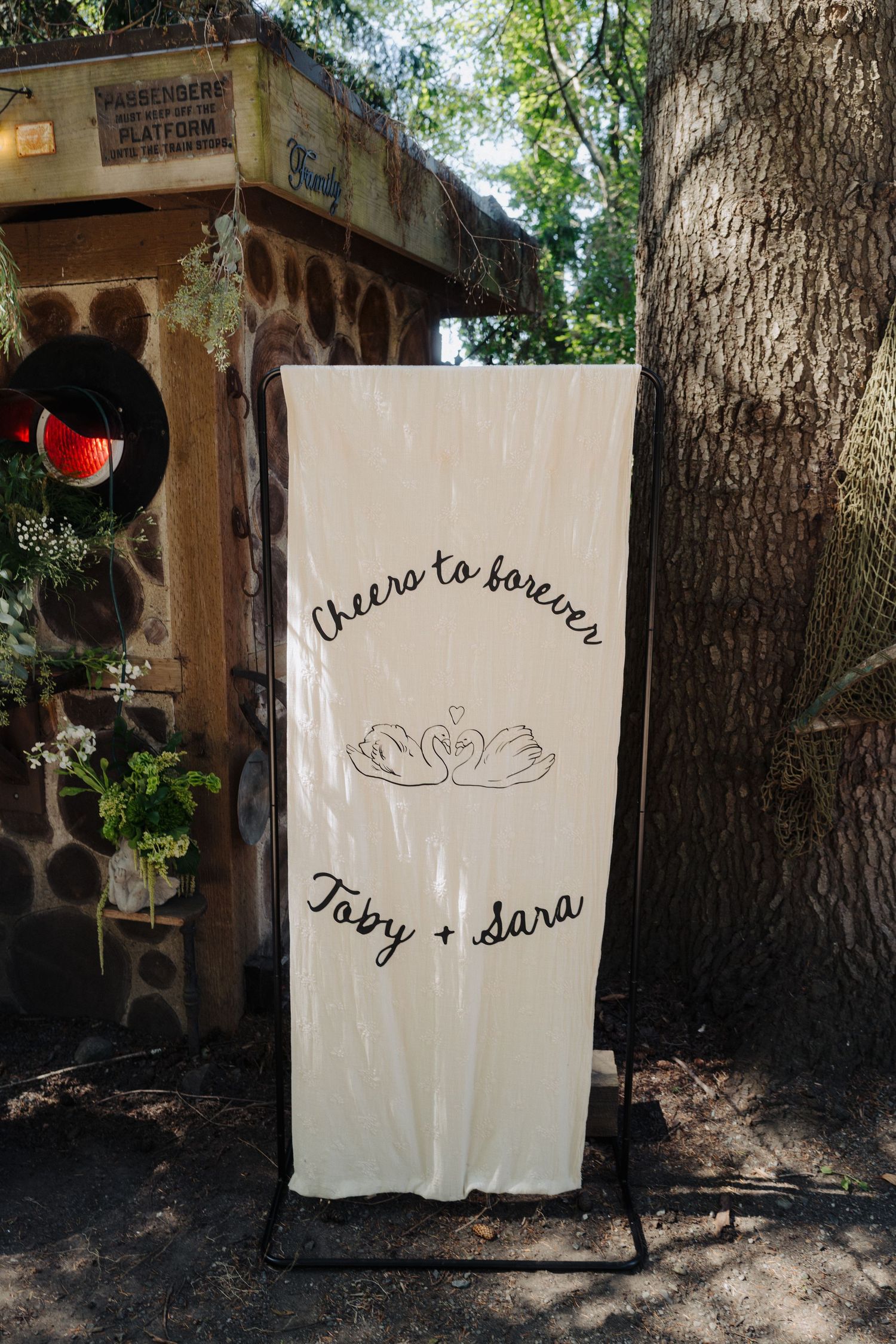 White fabric panels with handwritten names and text displayed against trees in an outdoor garden setting.