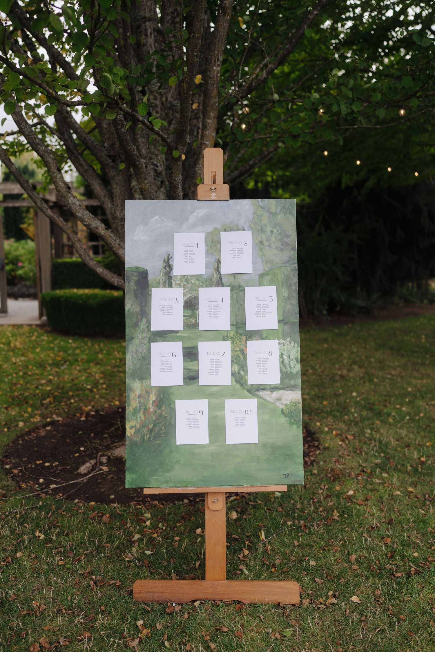 Garden wedding seating chart display with white paper cards mounted on green boards.