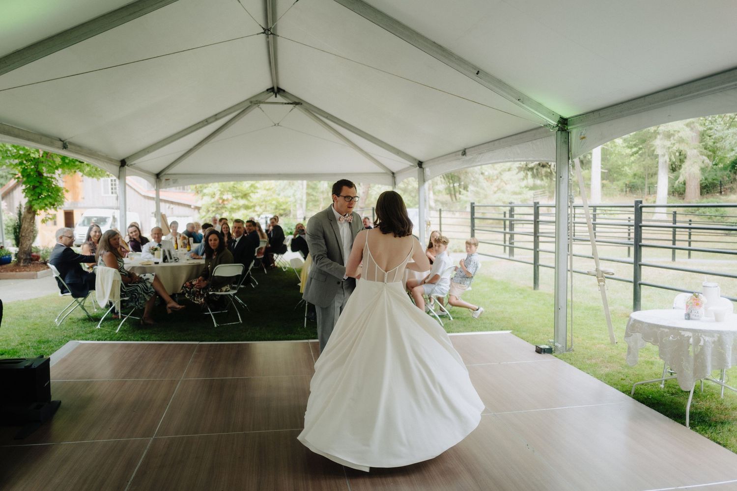 Wedding reception celebration under an elegant white tent with guests seated at tables for dinner.