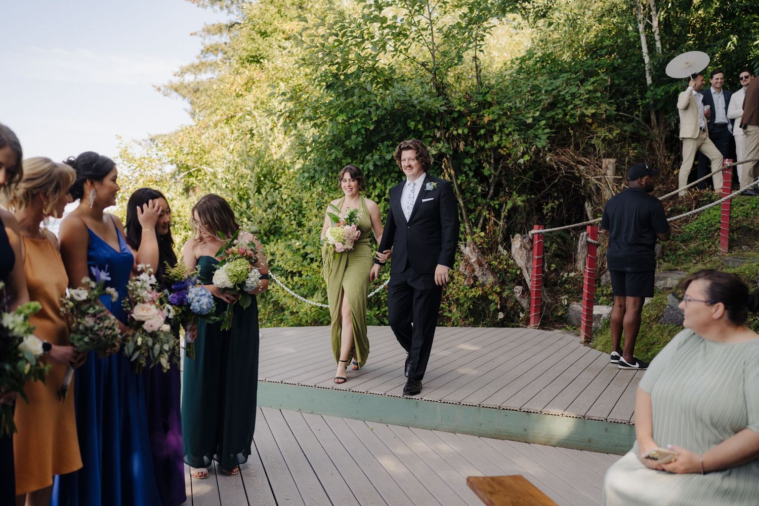 Wedding guests gather on a wooden deck during an outdoor ceremony.