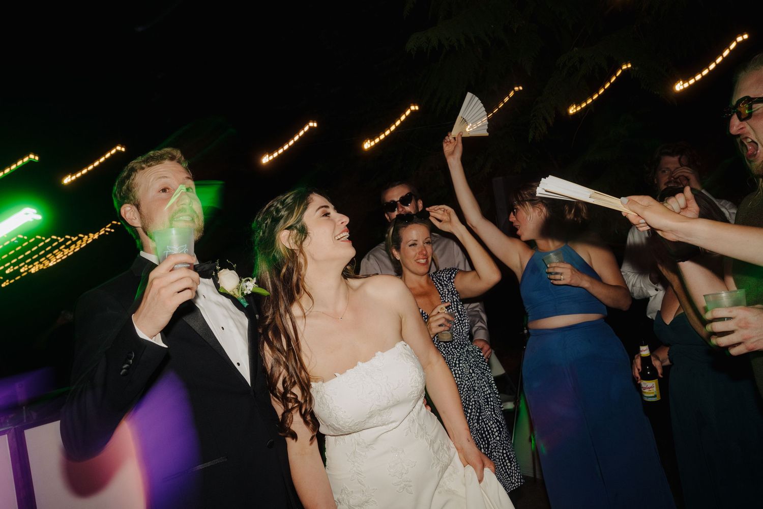 Wedding reception dance party with string lights and colorful lighting effects.