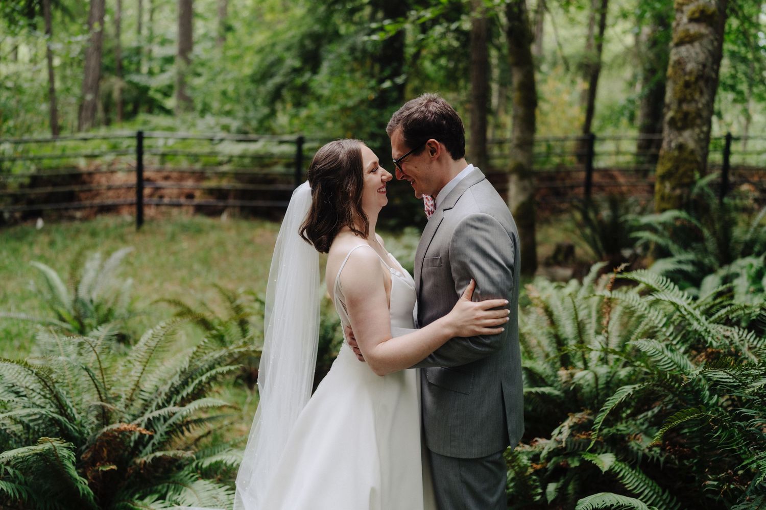 Newlyweds embrace among lush ferns in enchanting forest setting.