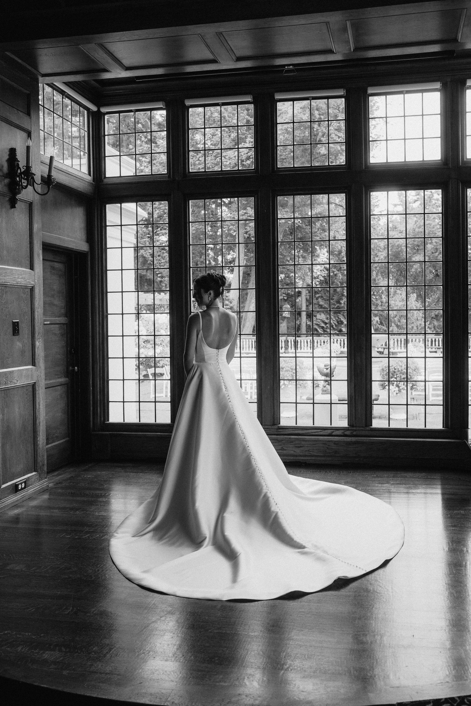Black and white photos of a wedding dress with dramatic train in a room with large windows.