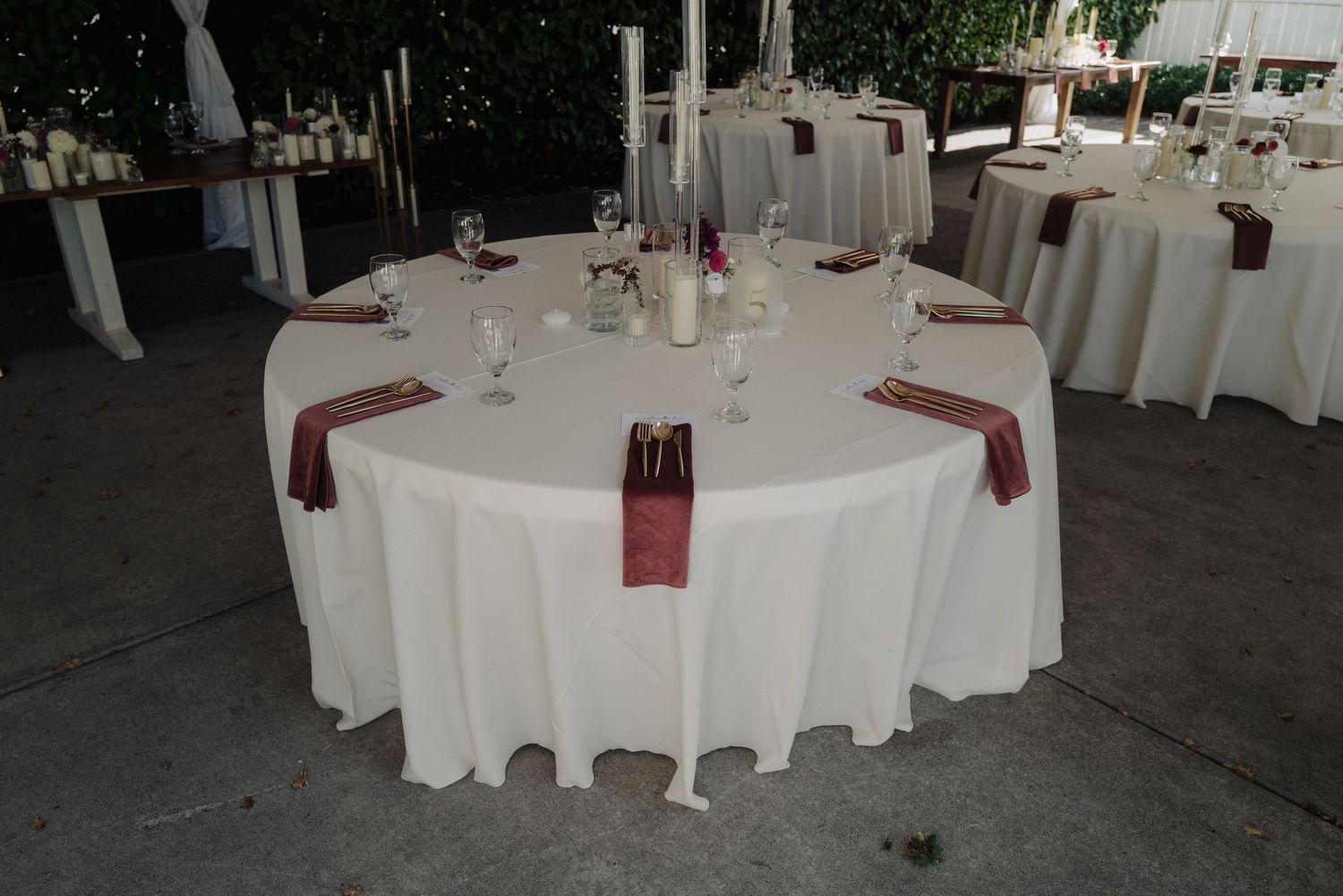 Elegant wedding reception table setting with white linens and burgundy napkins.