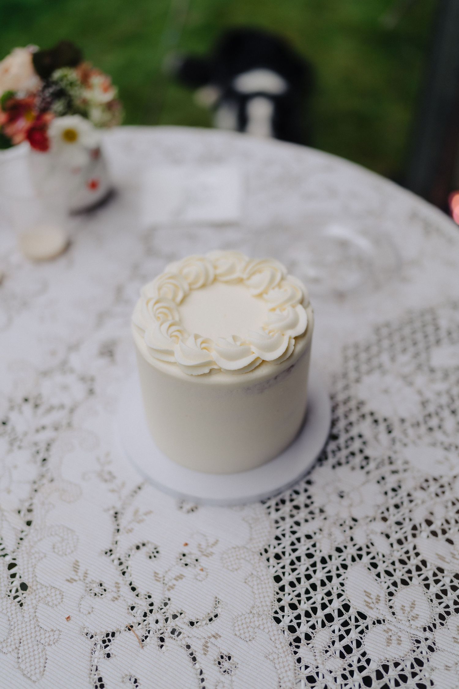 Small white wedding cake with delicate piped details sitting on a lace tablecloth.